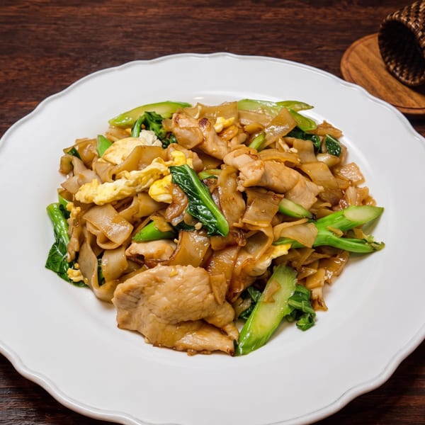 Pad See Ew with wide noodles, chicken, scrambled egg, and Chinese broccoli on a white plate.