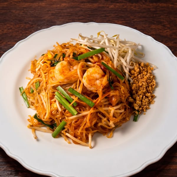 Shrimp Pad Thai with bean sprouts, green onions, and crushed peanuts on a white plate.
