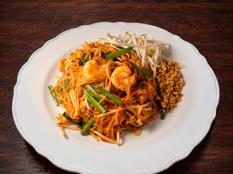 Shrimp Pad Thai with bean sprouts, green onions, and crushed peanuts on a white plate.